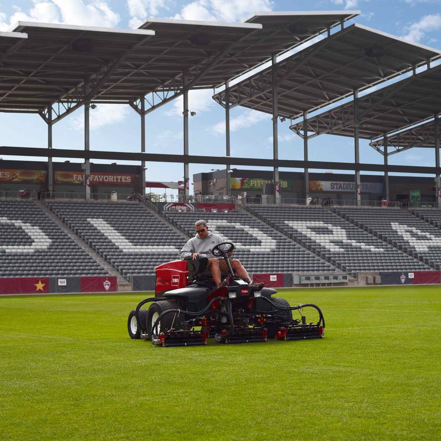 cm2009s_RM5410_Denver_037_1 sq Red ride-on mower in action on a well-maintained grass field with stadium seating in the background