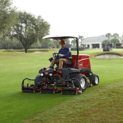 Red ride-on mower with a driver, cutting grass on a golf course, showcasing precision cutting units