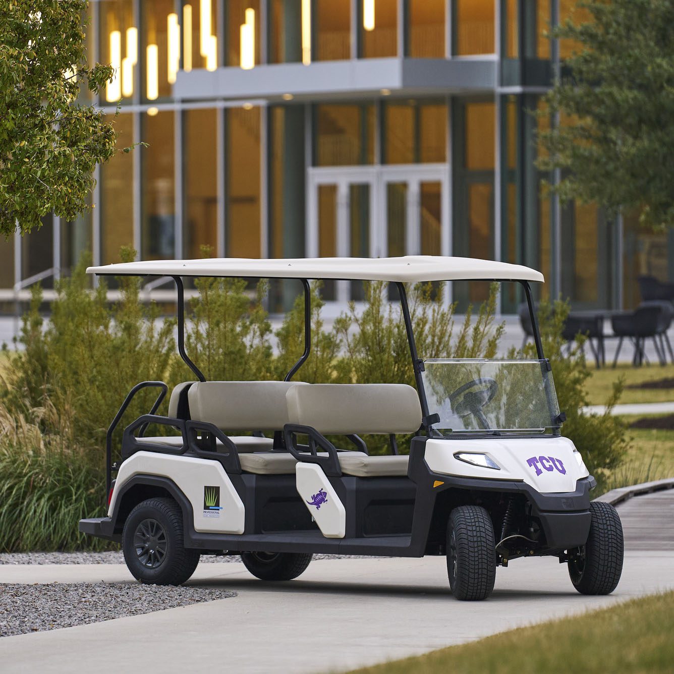 Toro Vista 4 golf cart with branding parked in front of modern building Front-side view of the Toro Vista 4 golf cart with decals, beige seats, and a sleek white exterior, parked in a landscaped area