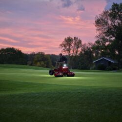 A person operates an electric greens roller on a golf course at sunset, highlighting its performance and design