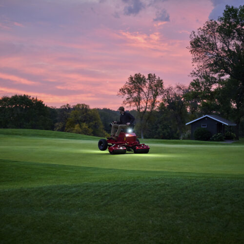 A person operates an electric greens roller on a golf course at sunset, highlighting its performance and design