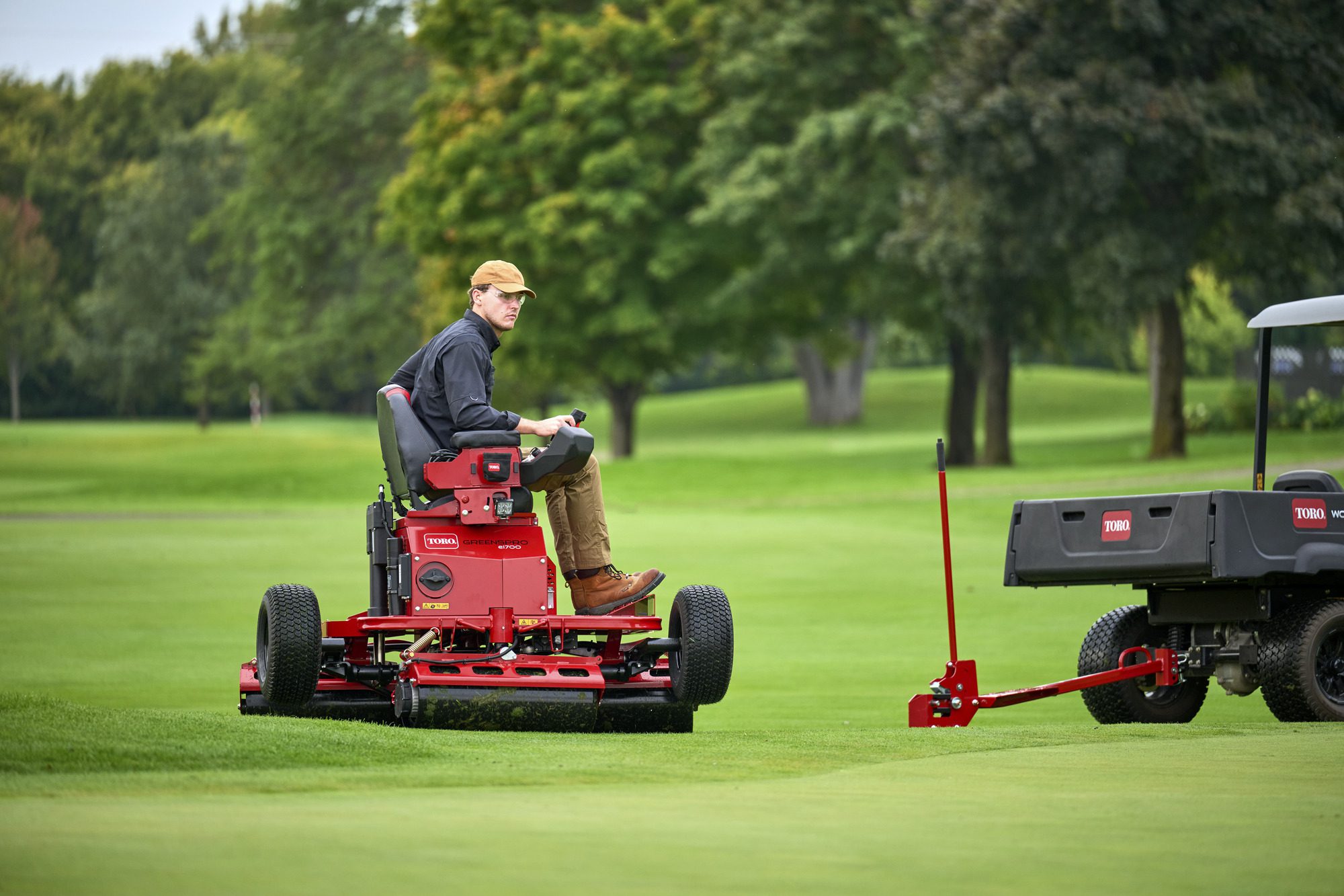 cm25_6197L_GreensPro_e1700_128 A person operates a red electric greens roller on a lush green golf course