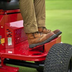 Close-up of a person’s feet on the red electric greens roller, showcasing its design and control features