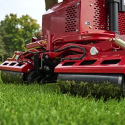 Close-up of a red electric greens roller on grass, showcasing its rollers and design features