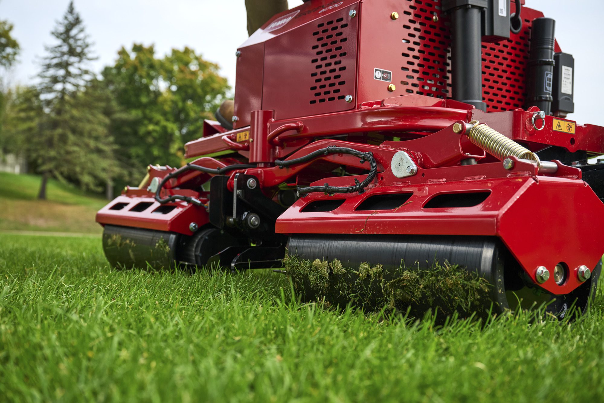 cm25_6197L_GreensPro_e1700_216 Close-up of a red electric greens roller on grass, showcasing its rollers and design features