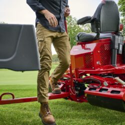 A person operates a red electric greens roller on a grassy field, showcasing its design and features