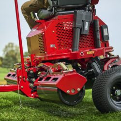 Close-up of a red electric greens roller with a rider, showcasing its design and key components on grass