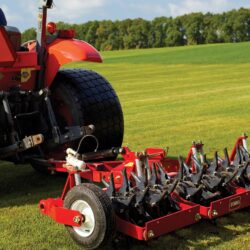 Red Toro aerator attached to a tractor, showing coring tines on a grassy field