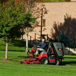 A rider mower in action on a grassy area, featuring a red and black design with a driver