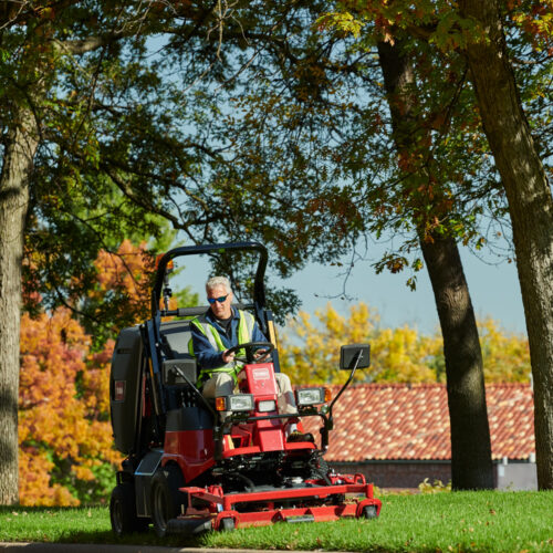 A rider mower in action, featuring a red and black design, with a driver among autumn trees