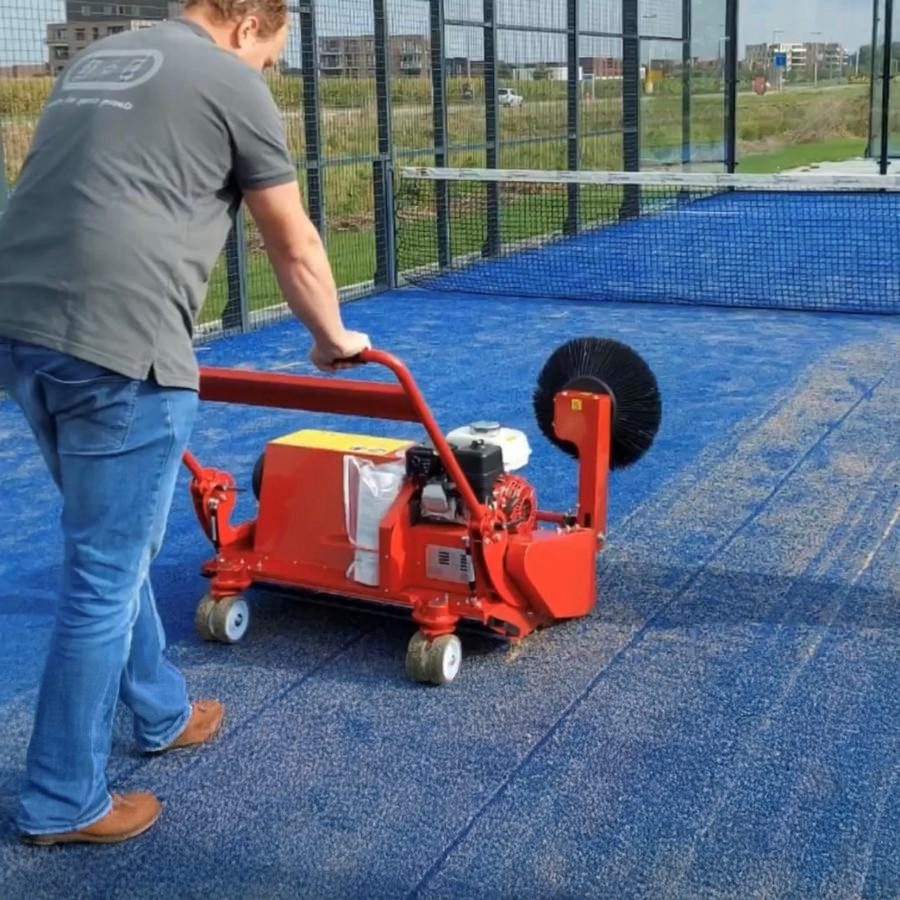 Operator using SMG TurfSoft TS3 artificial turf cleaner on blue turf SMG TurfSoft TS3 artificial turf cleaner being operated on blue turf, effectively sweeping debris with its large rotating brush.