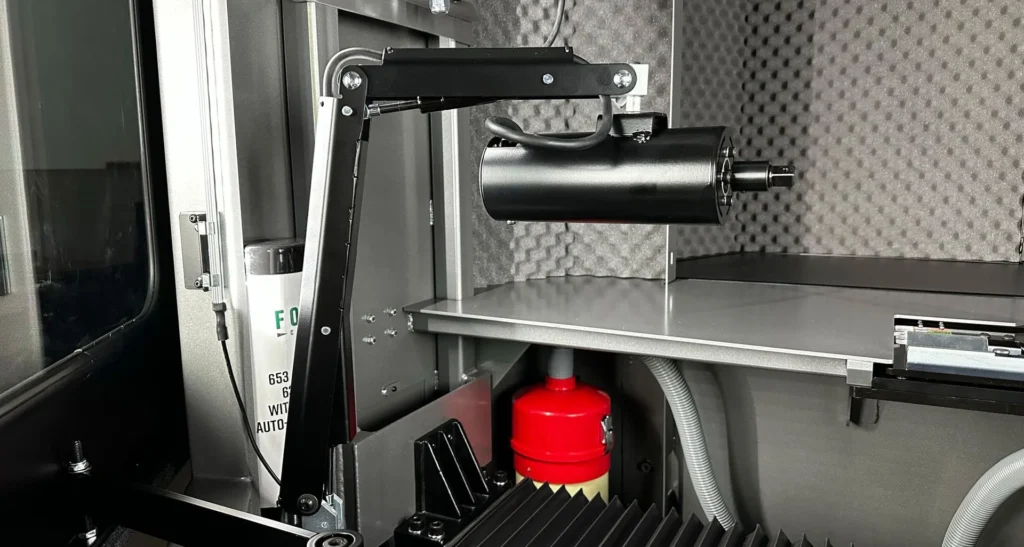 Close-up of a reel grinder's automated arm and safety enclosure with a red component visible