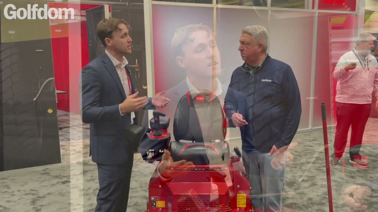 Two men discuss the Toro electric greens roller at a trade show, showcasing its features and design