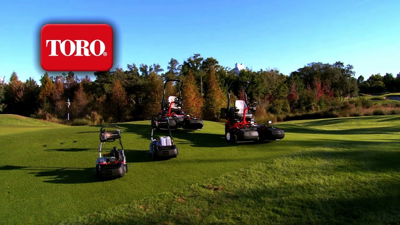 Multiple Toro lawn mowers are displayed on a green field under a clear blue sky