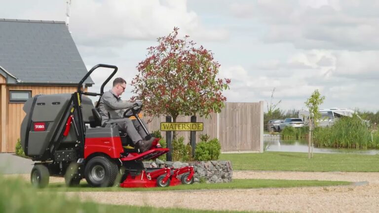 A person operates a Toro rotary mower on a landscaped lawn near a water feature