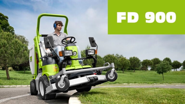 A man operates a green lawn mower on a curved path surrounded by trees and grass