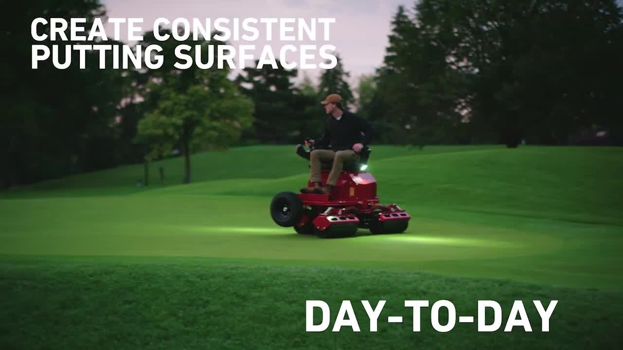 A person operates a red electric greens roller on a lush green golf course at dusk